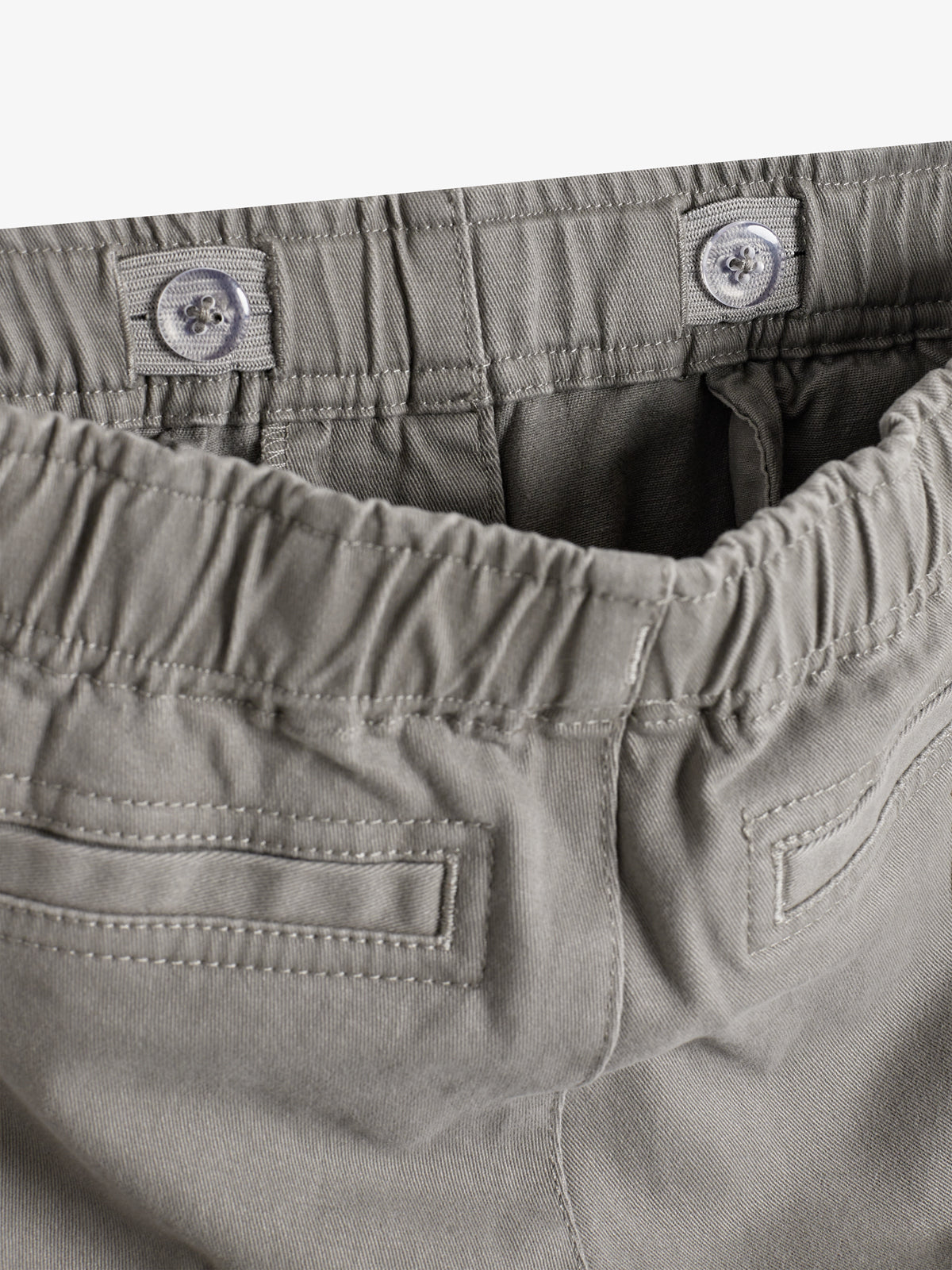 Graue Hose mit elastischem Bund und verstellbarem Knopfverschluss; zwei Gesäßtaschen. Sie liegt flach in einem hellen Umfeld.