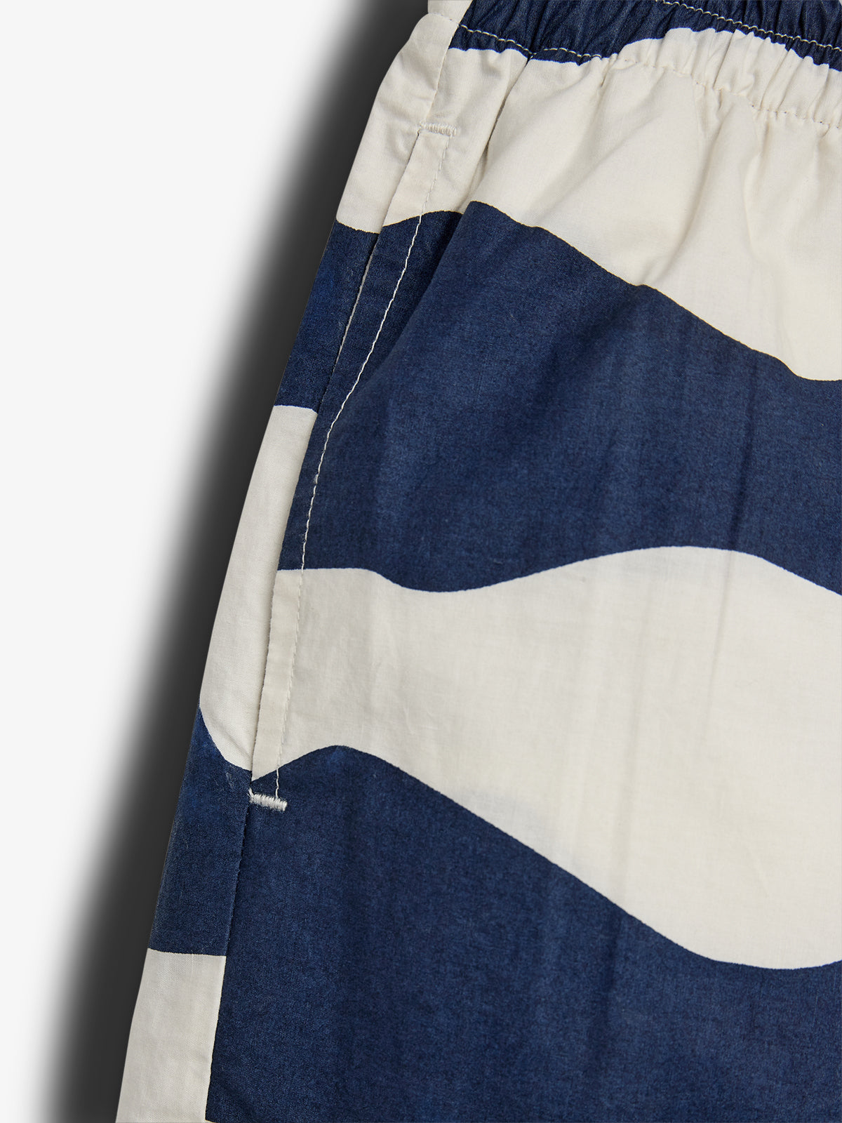 Navy and white patterned fabric displays a wavy design with a stitched border, forming part of an elastic waistband garment, likely shorts or pants, against a plain background.
