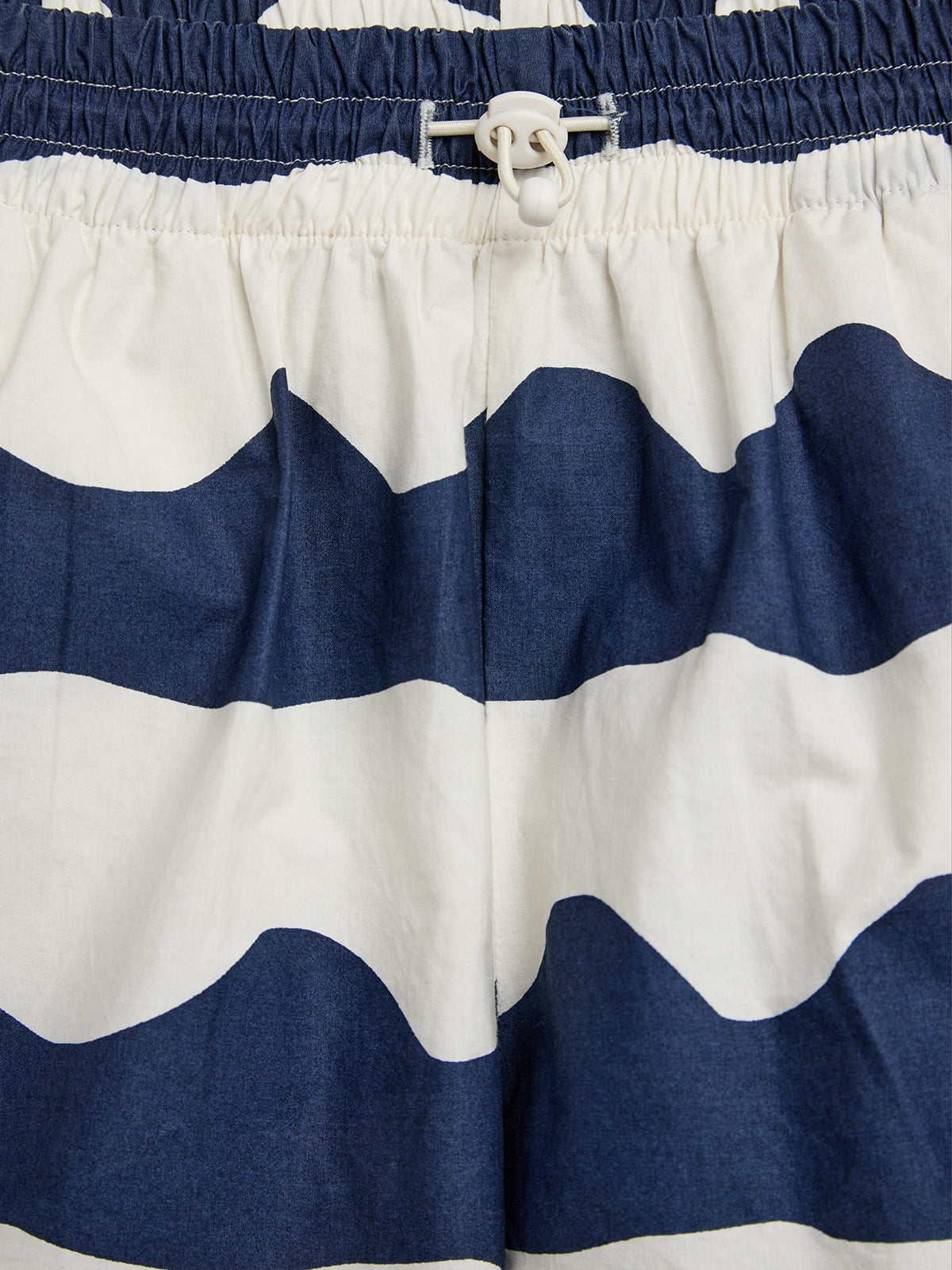 Shorts displaying navy and white wavy stripes. A white plastic clasp secures the elastic waistband. The fabric is gathered at the waist, suggesting a relaxed fit.