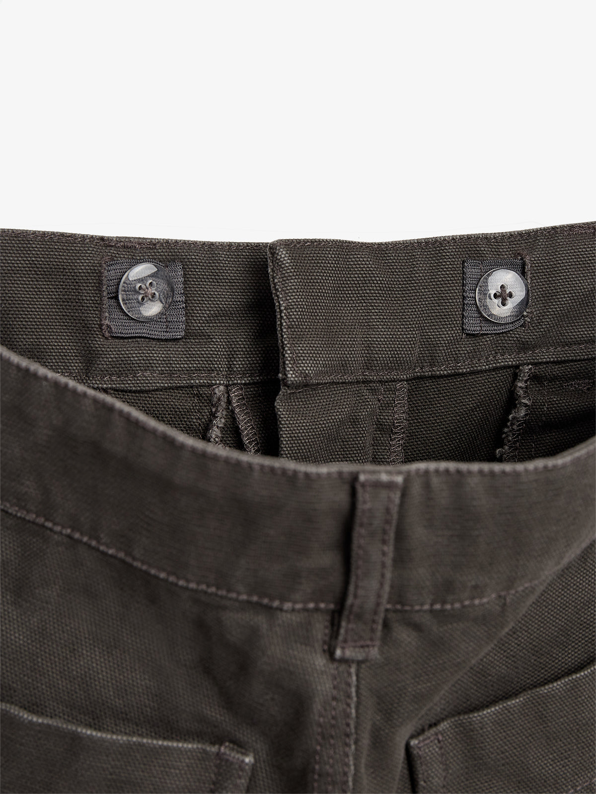 Dark fabric pants display two buttons and stitching at the waistband, viewed from above, against a plain background.
