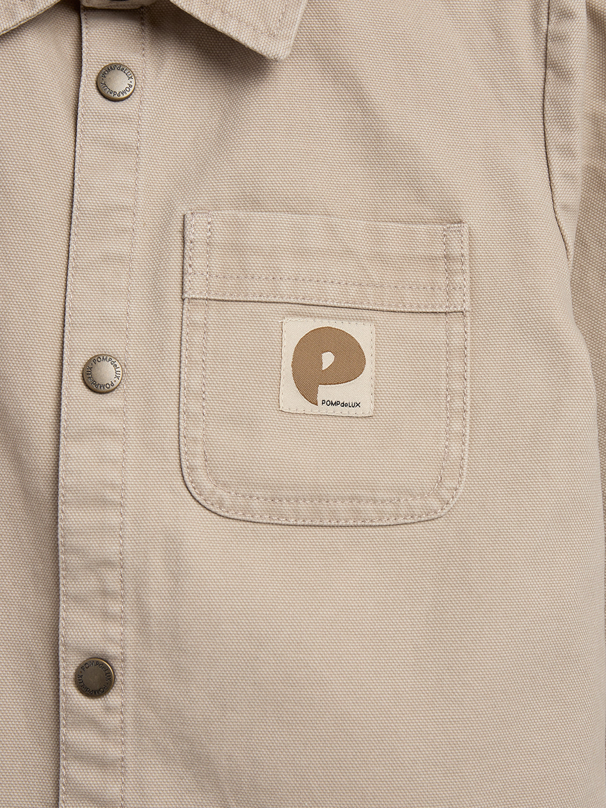 Beige shirt pocket displays a logo tag with a brown and white design. Metal buttons inscribed with "POWERHUNK" line the shirt's placket. The fabric appears as part of casual attire.