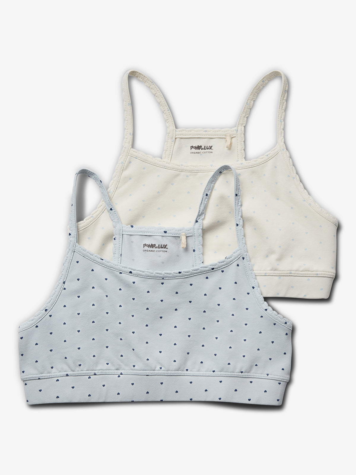 Two soft cotton bralettes are layered; one light blue with small heart patterns, the other off-white with similar patterns. Both display the text: "POMPdeLUX ORGANIC COTTON" on tags.