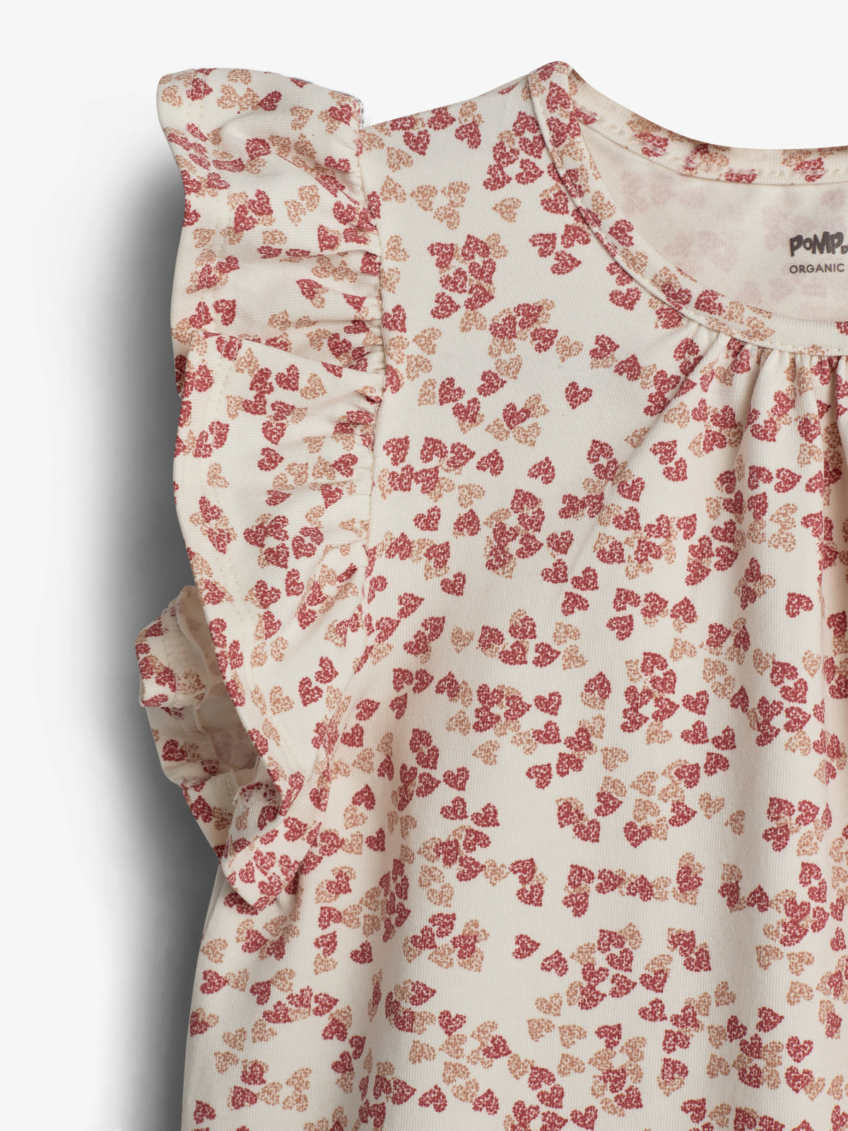 A cream-colored, short-sleeve dress features a red floral pattern with ruffled sleeves. The fabric is soft, likely cotton, and labeled "PomPom Organic" inside, providing a sense of eco-friendly production.