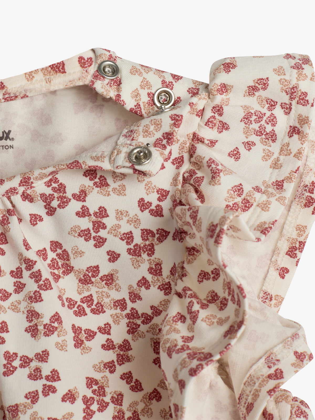 A floral-printed fabric with small reddish-brown patterns, featuring metal snap buttons in a folded section. The material is decorated with ruffled edges, creating a soft, delicate appearance.