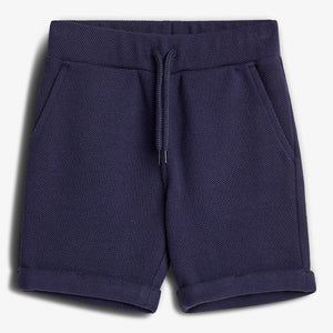 Dark blue shorts lie flat, featuring a textured fabric, drawstring waist, and pockets. They have folded cuffs, placed against a plain white background.