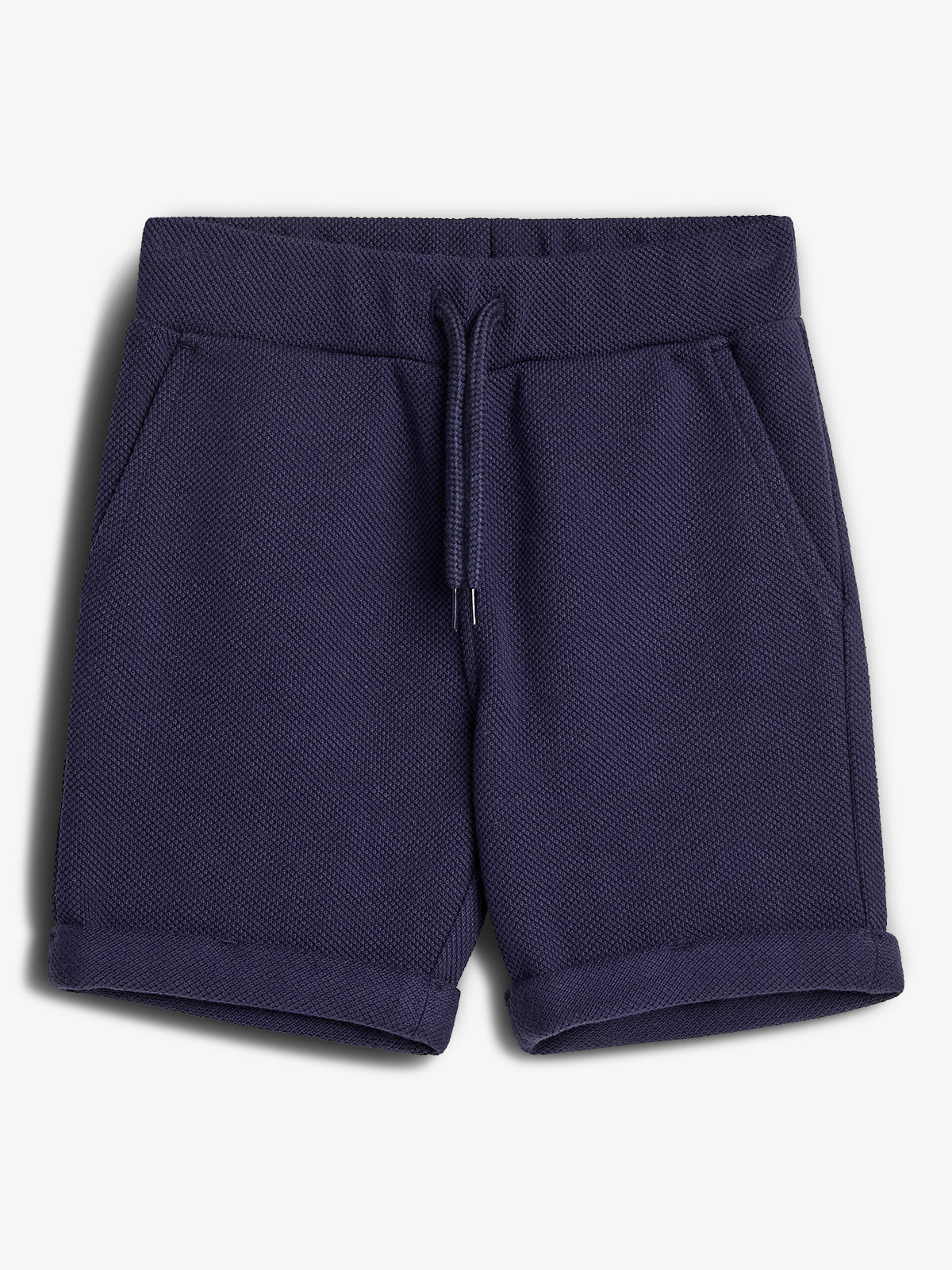 Dark blue shorts lie flat, featuring a textured fabric, drawstring waist, and pockets. They have folded cuffs, placed against a plain white background.