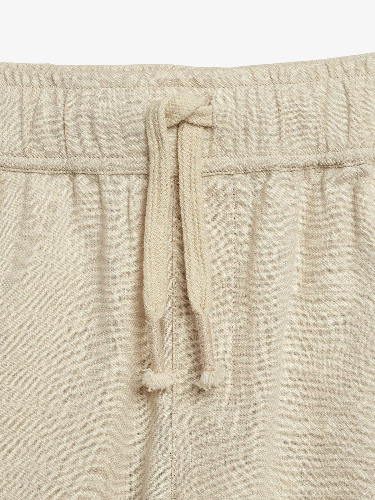 Beige drawstring pants feature a tied cord at the waistband. The fabric appears textured and soft, suitable for casual wear, with gentle folds indicating a relaxed fit.