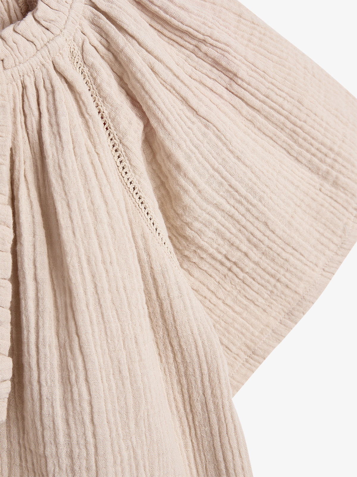 Beige, textured fabric hangs, showing detailed pleats and subtle seam lines. The material appears soft and crinkled, set against a plain white background.