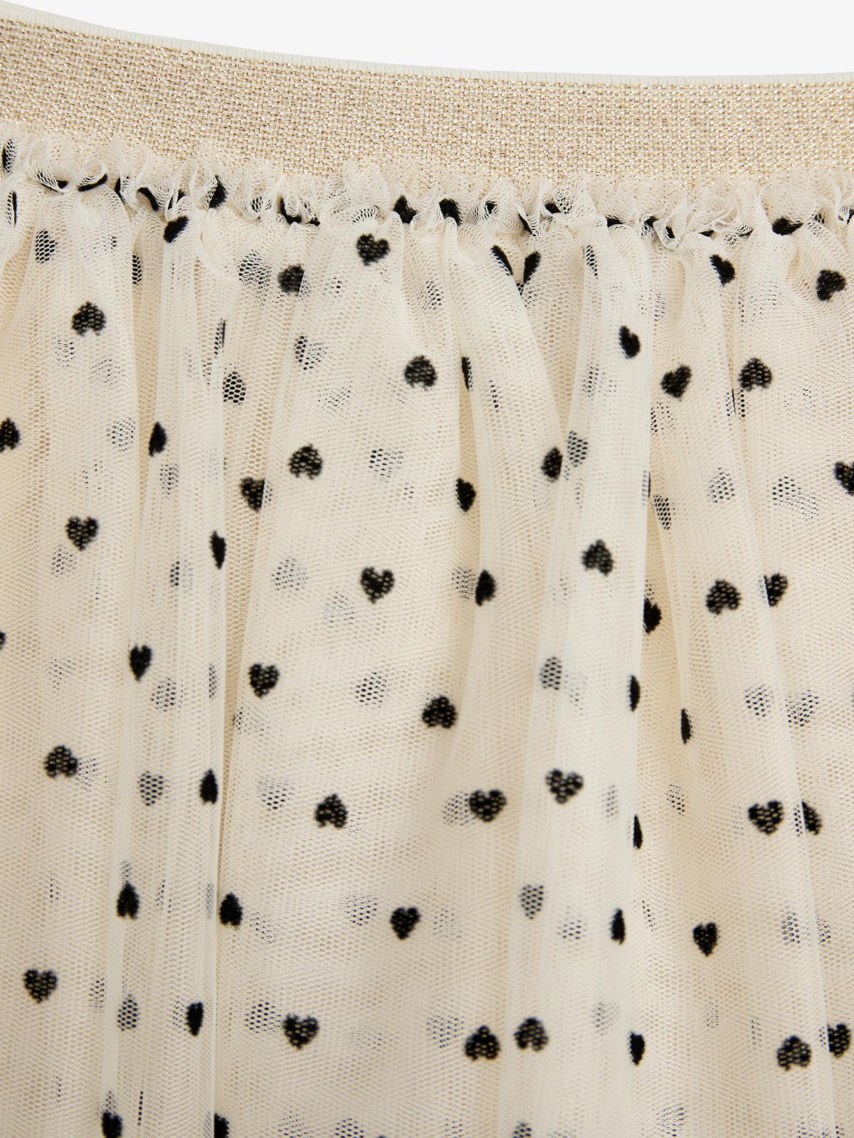 A fabric features a gold elastic waistband and sheer white material adorned with small black heart patterns, creating a delicate, whimsical design.