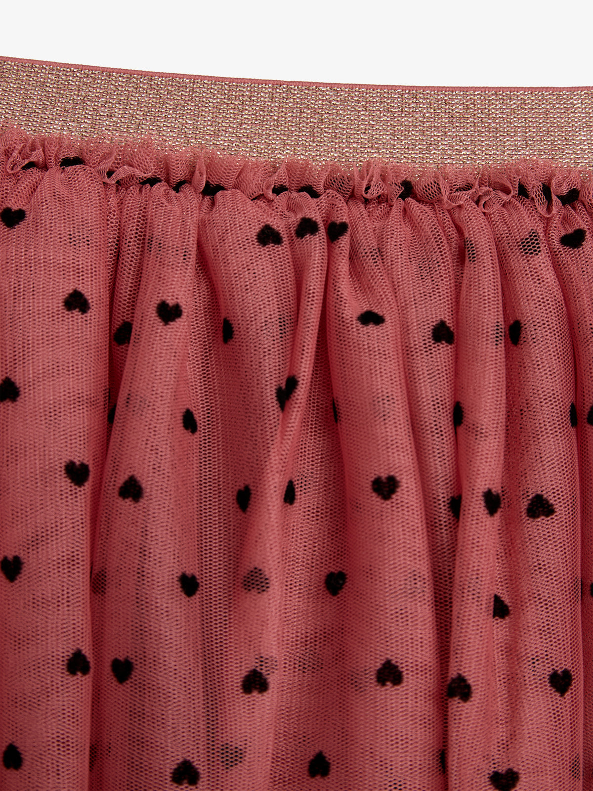 A pink tulle fabric features small black heart patterns, gathered under a glittery, textured waistband, suggesting its use as part of a skirt or dress.