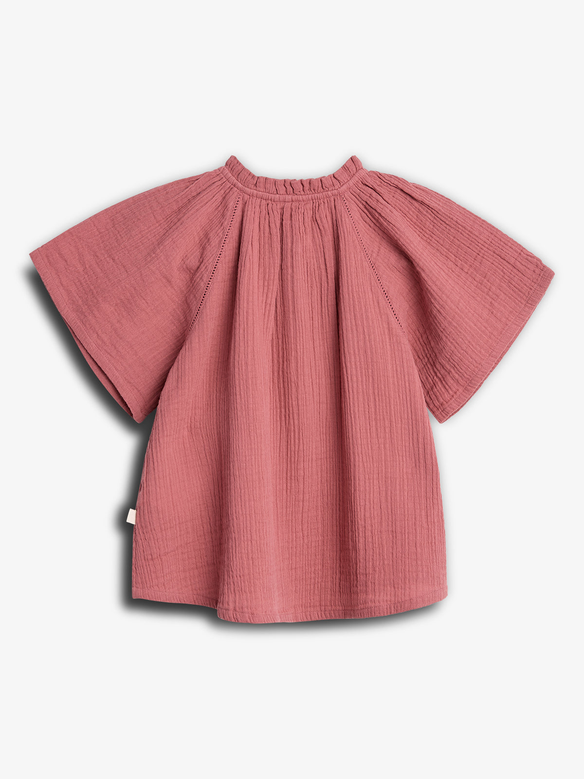 A pink, short-sleeved, textured shirt is displayed on a plain white background, showcasing its billowy, relaxed fit and loose round neckline. No text is present.