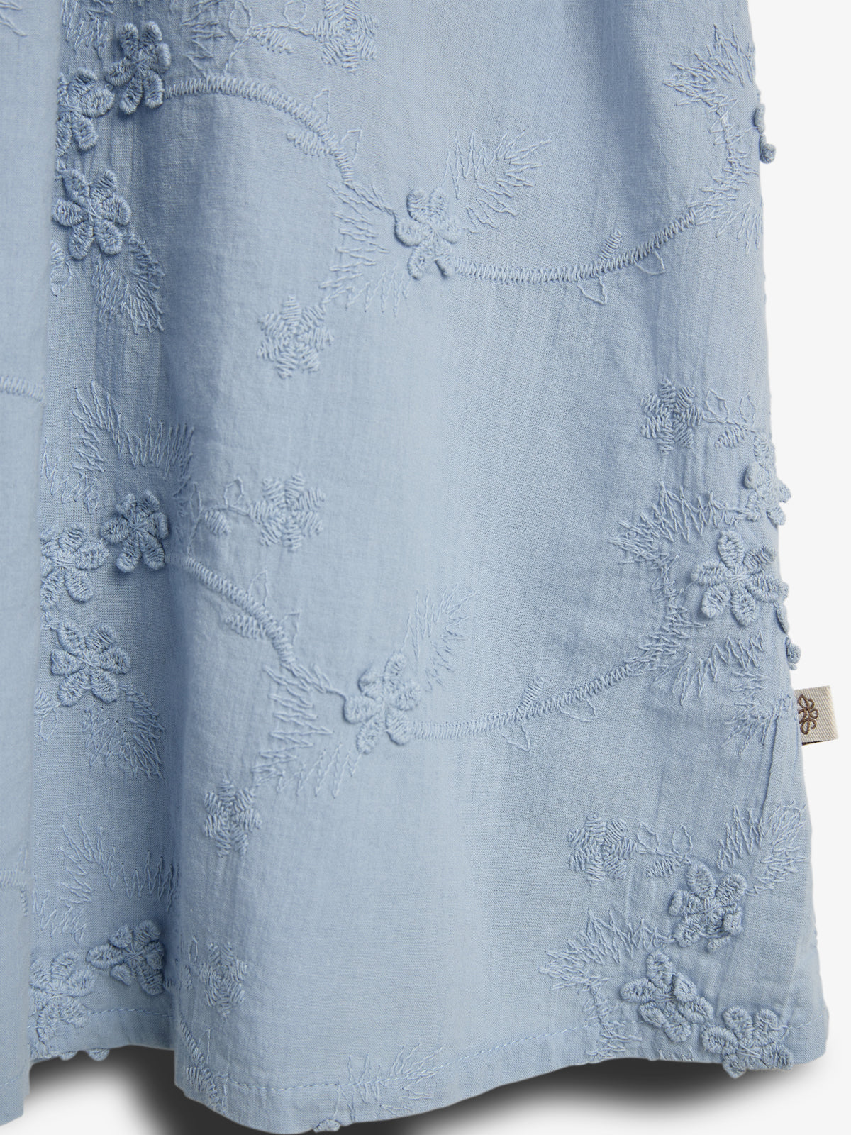 Blue fabric features intricate floral embroidery with raised patterns and textured designs. The textile has a soft, flowing appearance, suggesting a draped garment in an elegant and delicate style.