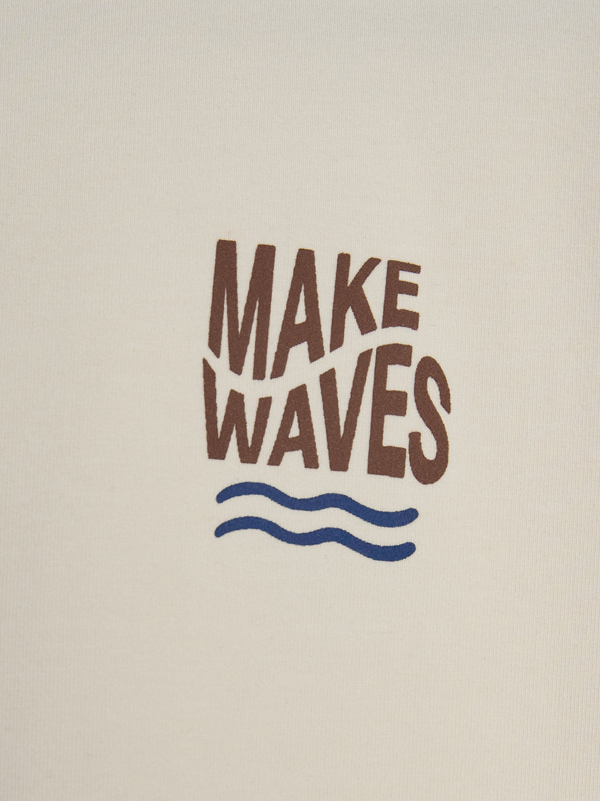Text "MAKE WAVES" is written in bold brown letters above two blue wavy lines, centered on a beige fabric background.