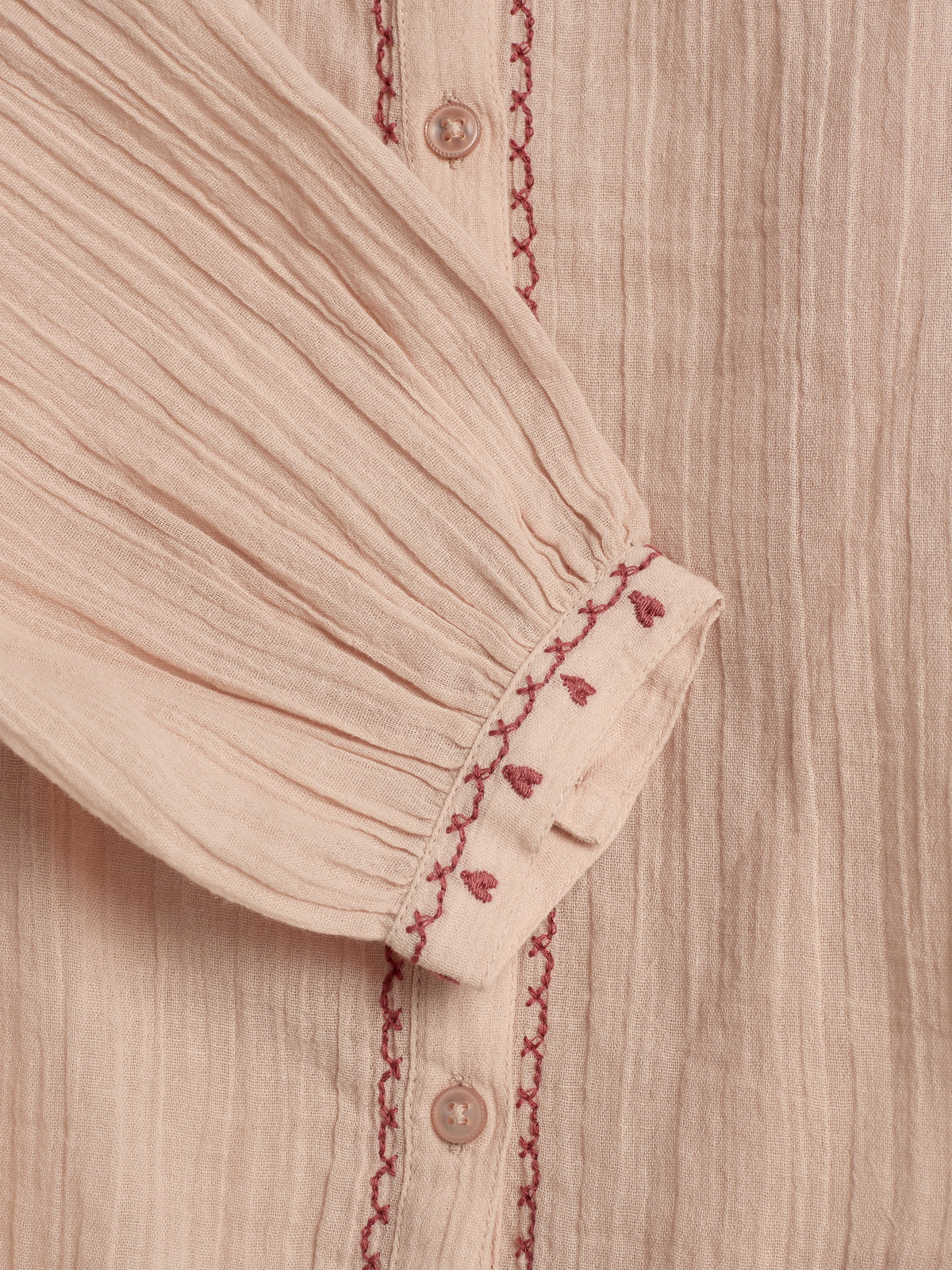 A beige fabric with red embroidered accents and pleated texture. A vertical row of buttons runs beside the embroidery, creating a decorative, textured look.