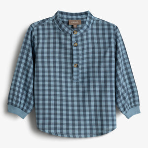 Ein langärmeliges, blau kariertes Hemd mit Rundkragen und drei Knöpfen vorne hängt vor einem weißen Hintergrund. Beschriftung "POMPdeLUX".