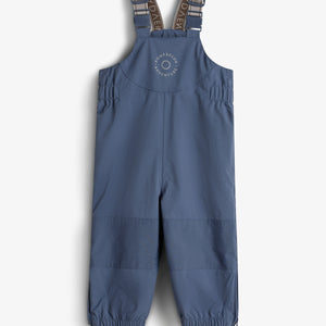 Eine blaue Kinderregenhose mit verstellbaren Trägern ist auf einem neutralen Hintergrund dargestellt. Auf der Brust steht: "ROMPDE LUX ADVENTURE".