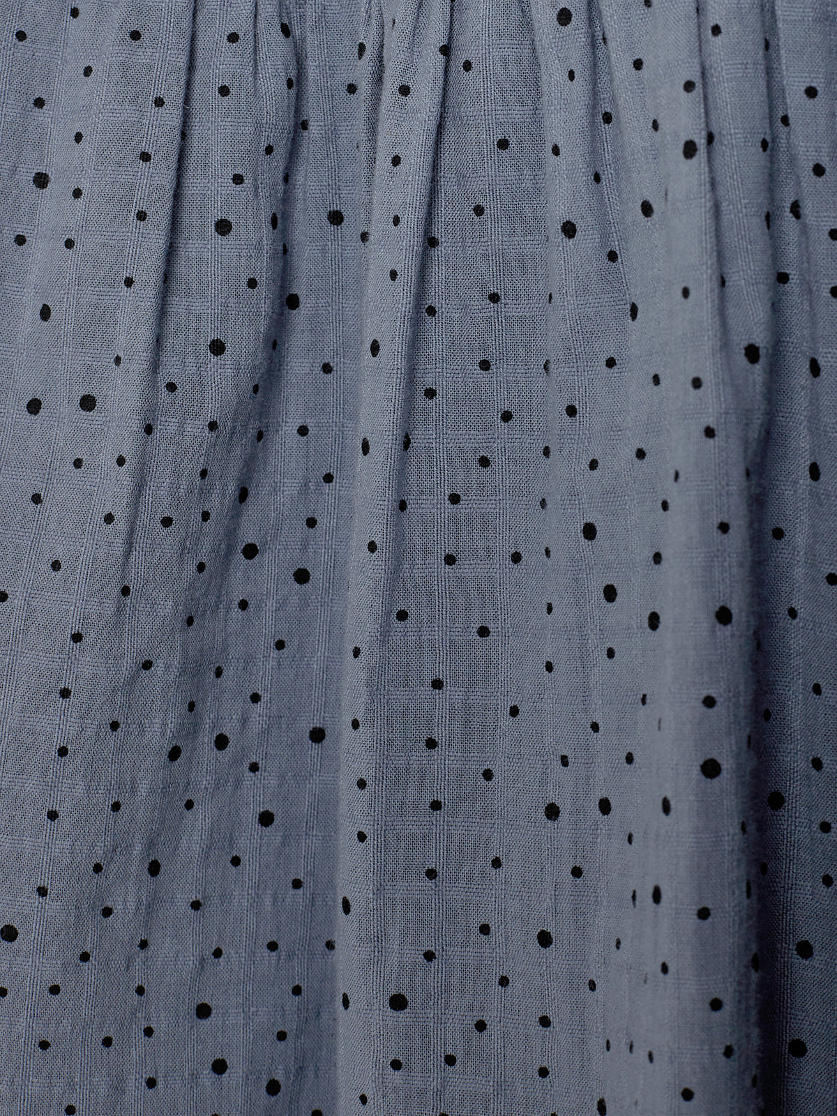 Gray fabric features a pattern of black polka dots, with soft pleats creating a textured appearance. The fabric's background shows a subtle checkered weave, adding depth and interest.