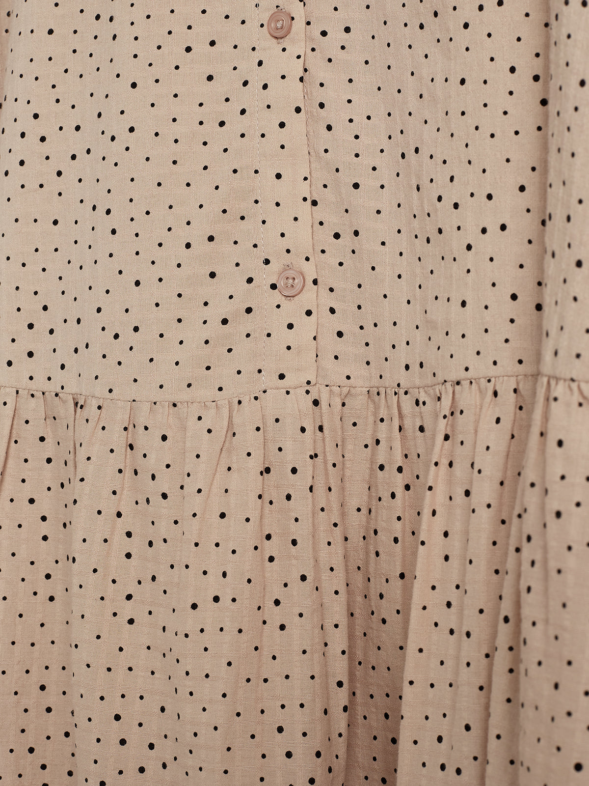 A beige fabric with black polka dots features two small buttons along a vertical seam, with slight gathering near the bottom edge. The pattern creates a simple, textured appearance.