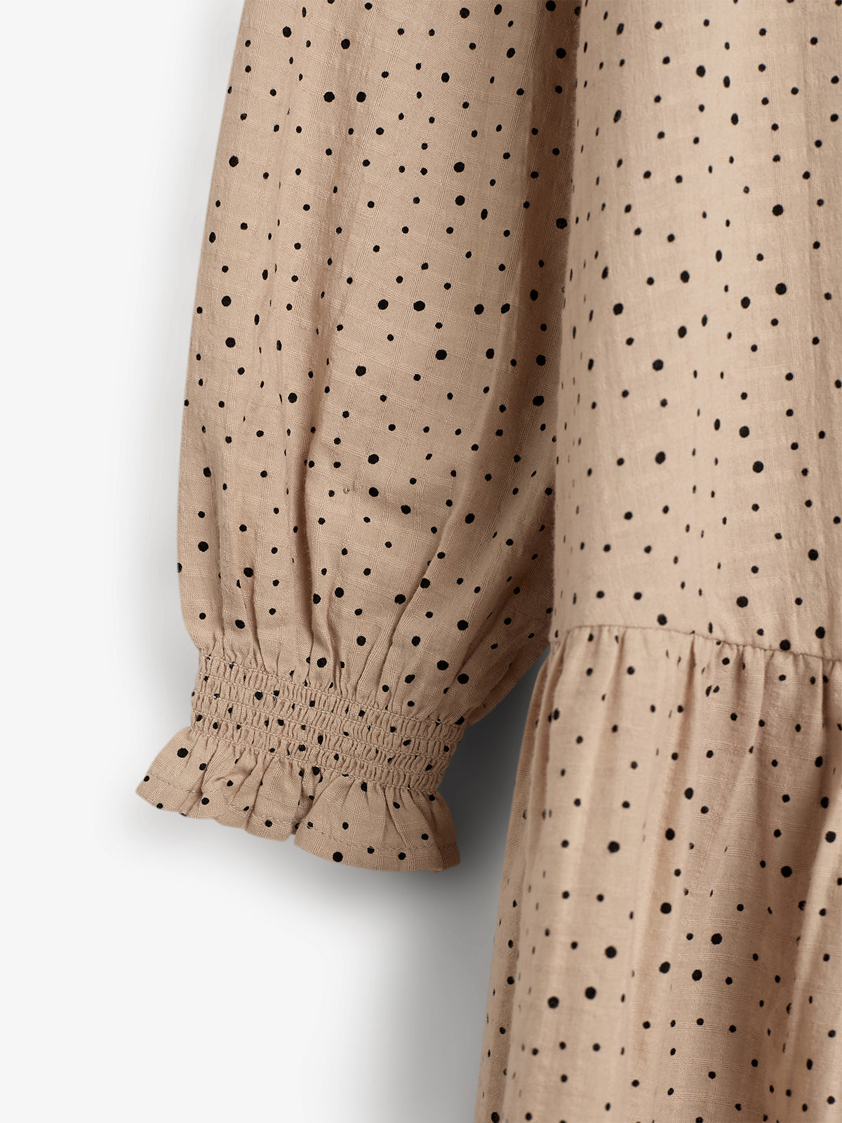A beige, long-sleeved fabric showcases black polka dots, featuring gathered cuffs and a ruffled trim. It appears to be part of a dress or blouse, photographed against a plain background.