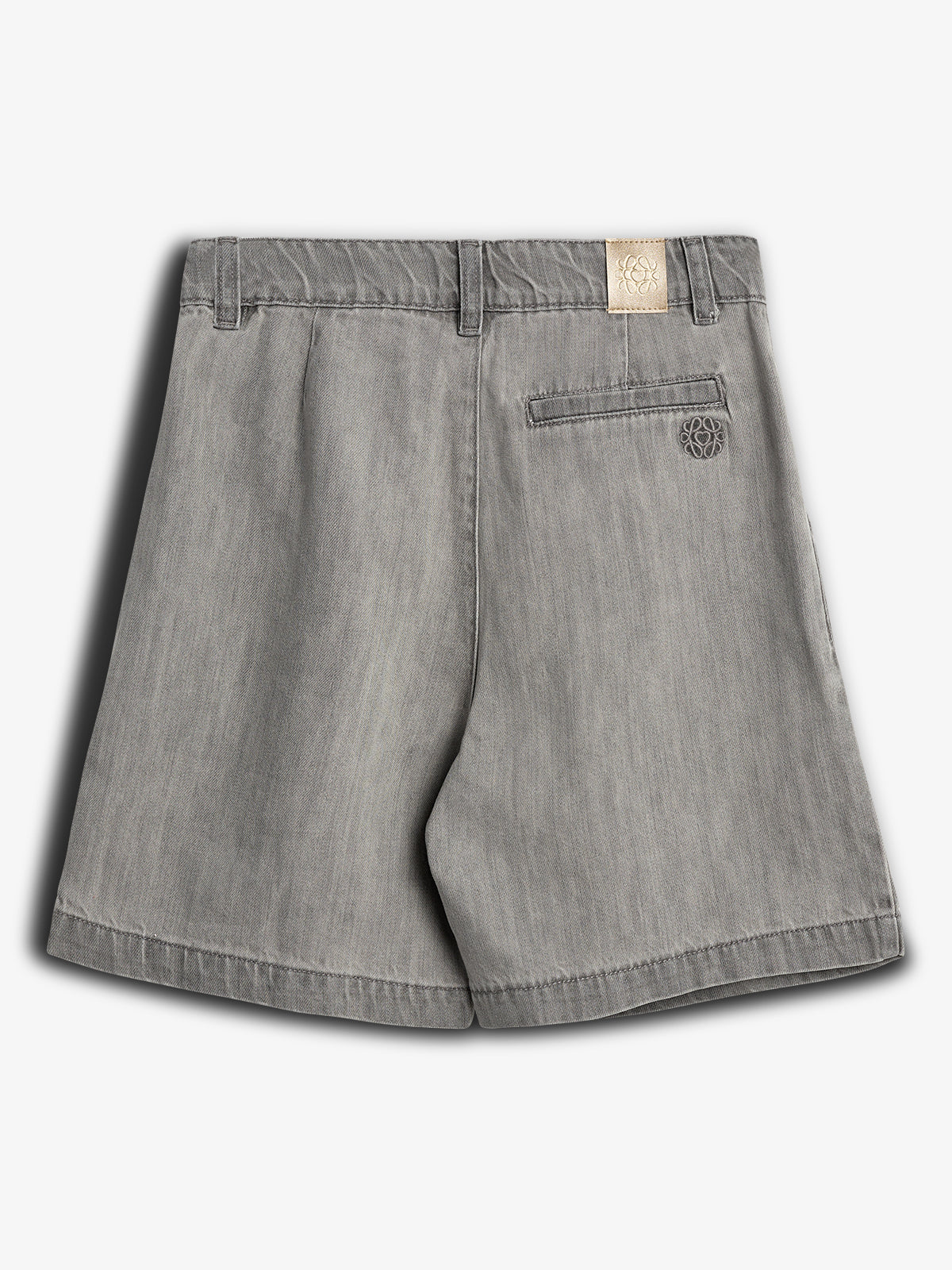 Gray shorts hanging against a neutral background, featuring belt loops and a single back pocket with embroidered design. A small beige tag with an intricate logo is attached at the waistband.