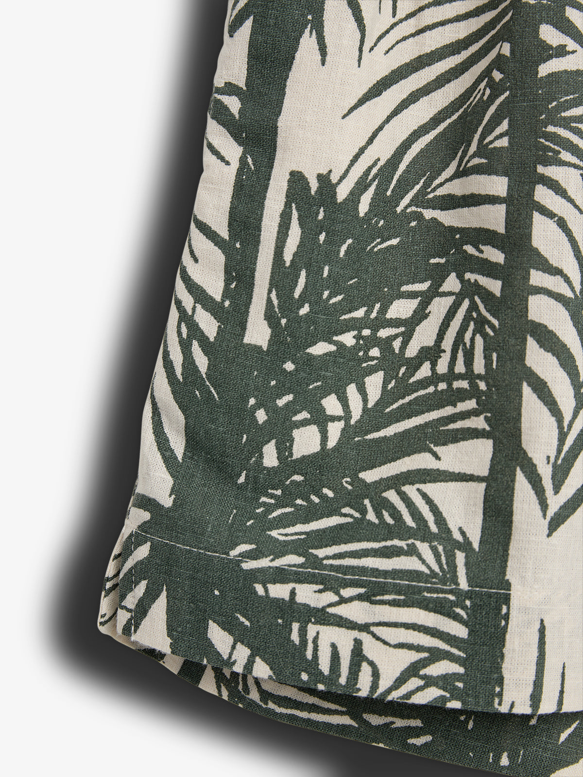 Fabric with a green botanical print, featuring silhouetted leaves and stems, draped against a light background, casting a soft shadow on the surface below.