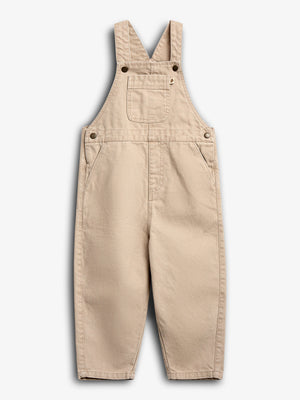Beige overalls hang against a white background, featuring adjustable shoulder straps, a chest pocket, and side pockets, emphasizing a classic design with visible metal buttons for fastening.