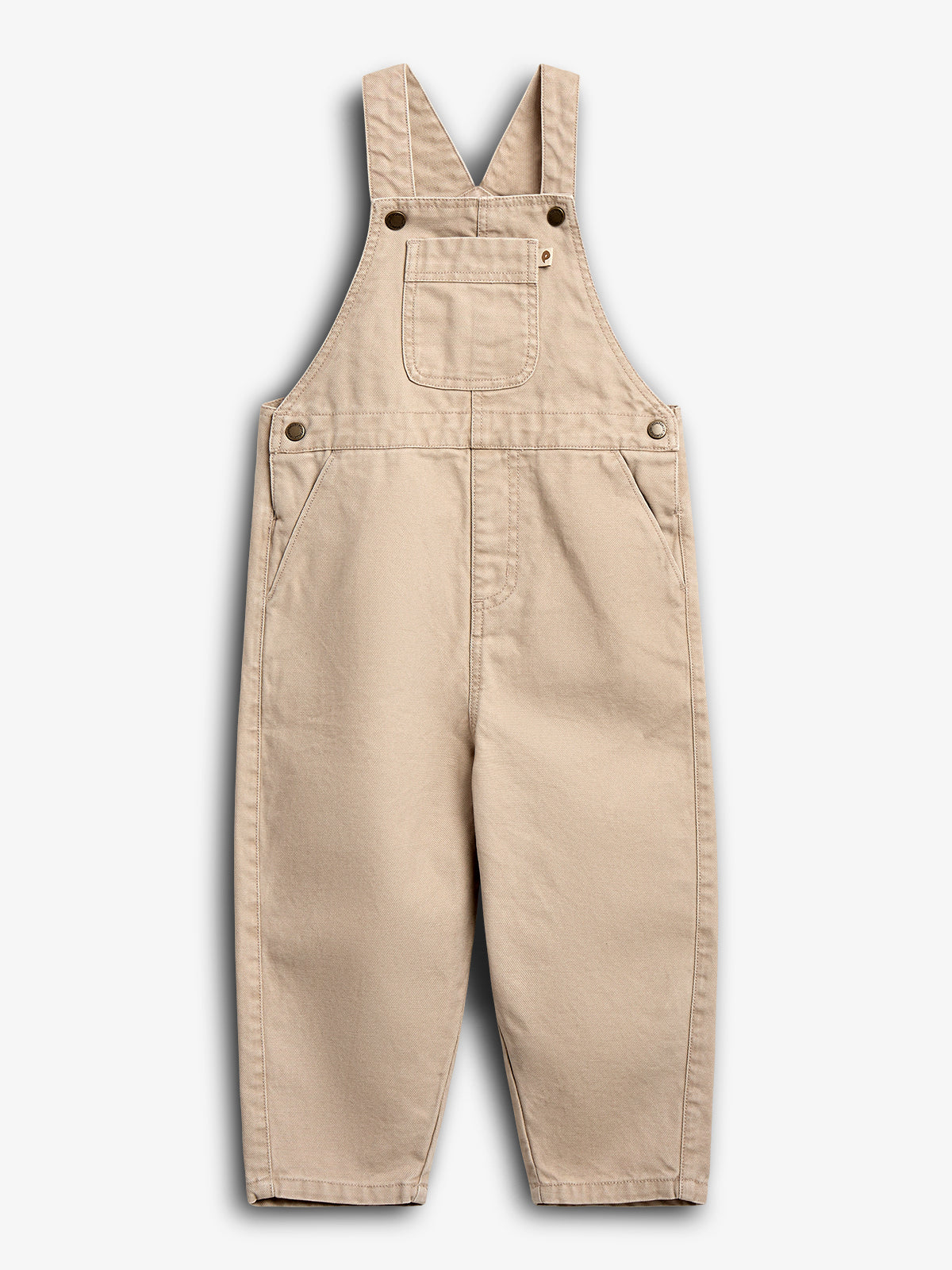 Beige overalls hang against a white background, featuring adjustable shoulder straps, a chest pocket, and side pockets, emphasizing a classic design with visible metal buttons for fastening.