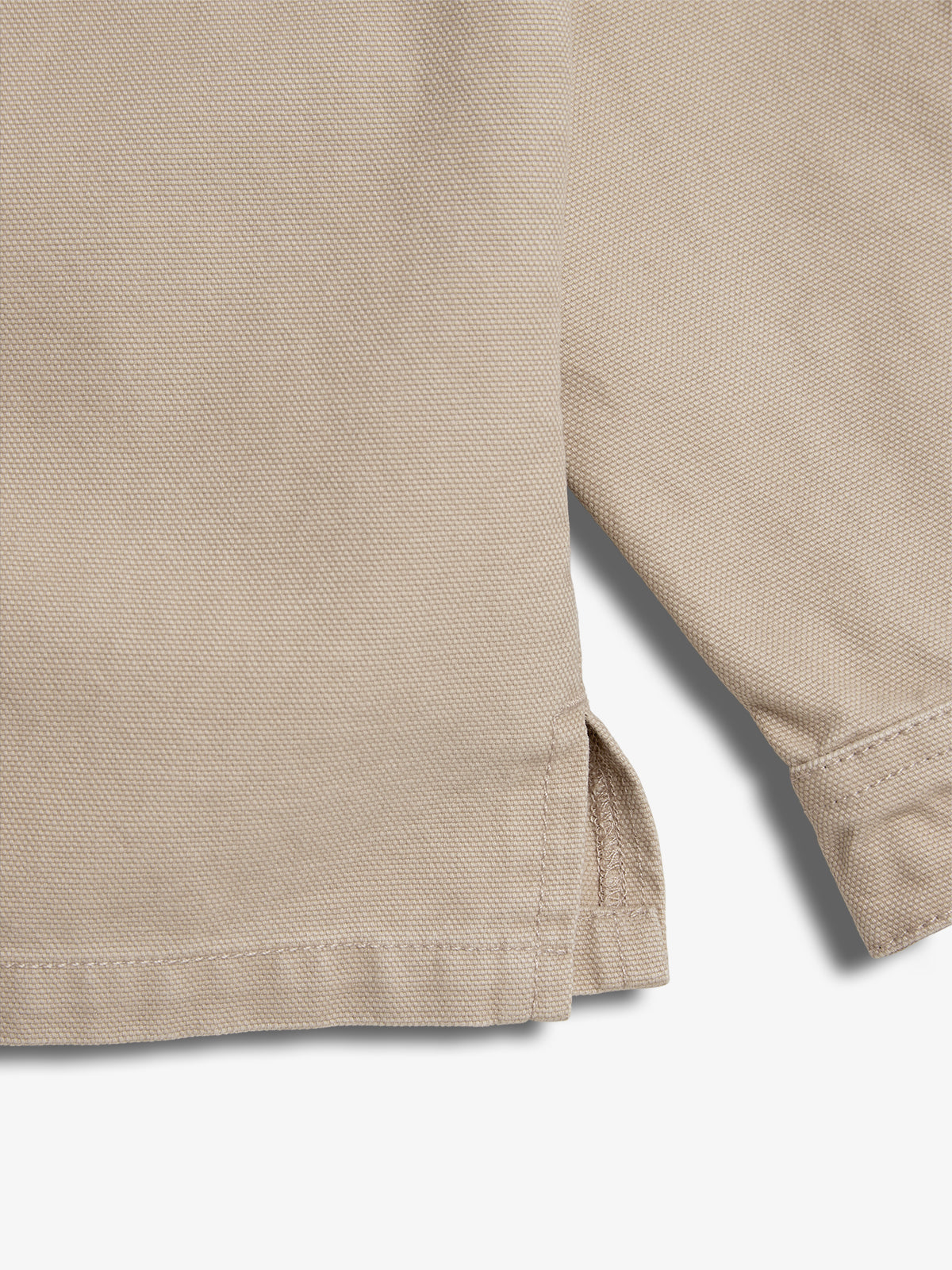 Beige fabric with a textured weave and visible hem stitching features a small side slit. The fabric is laid flat on a neutral background.