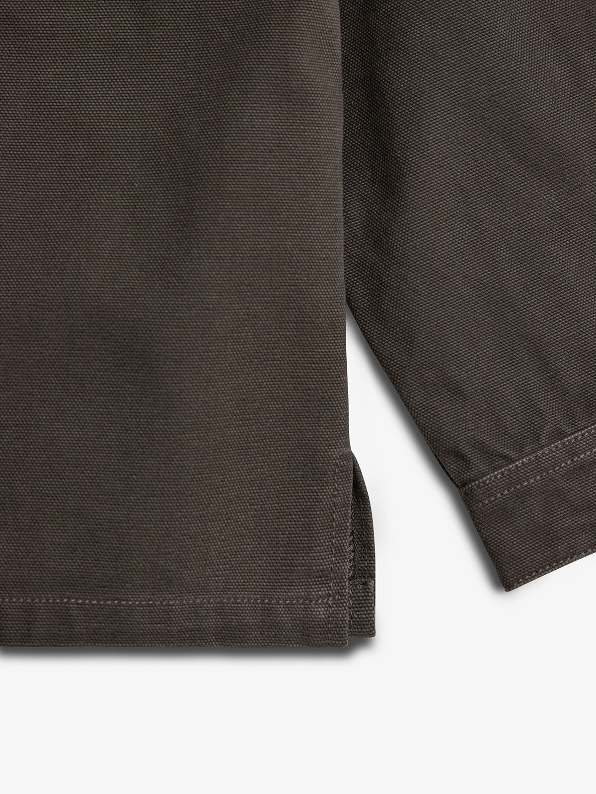 Dark fabric with textured stitching forms the corner of a flat surface, showing intersecting seams and a small hemline slit. The background is plain white.