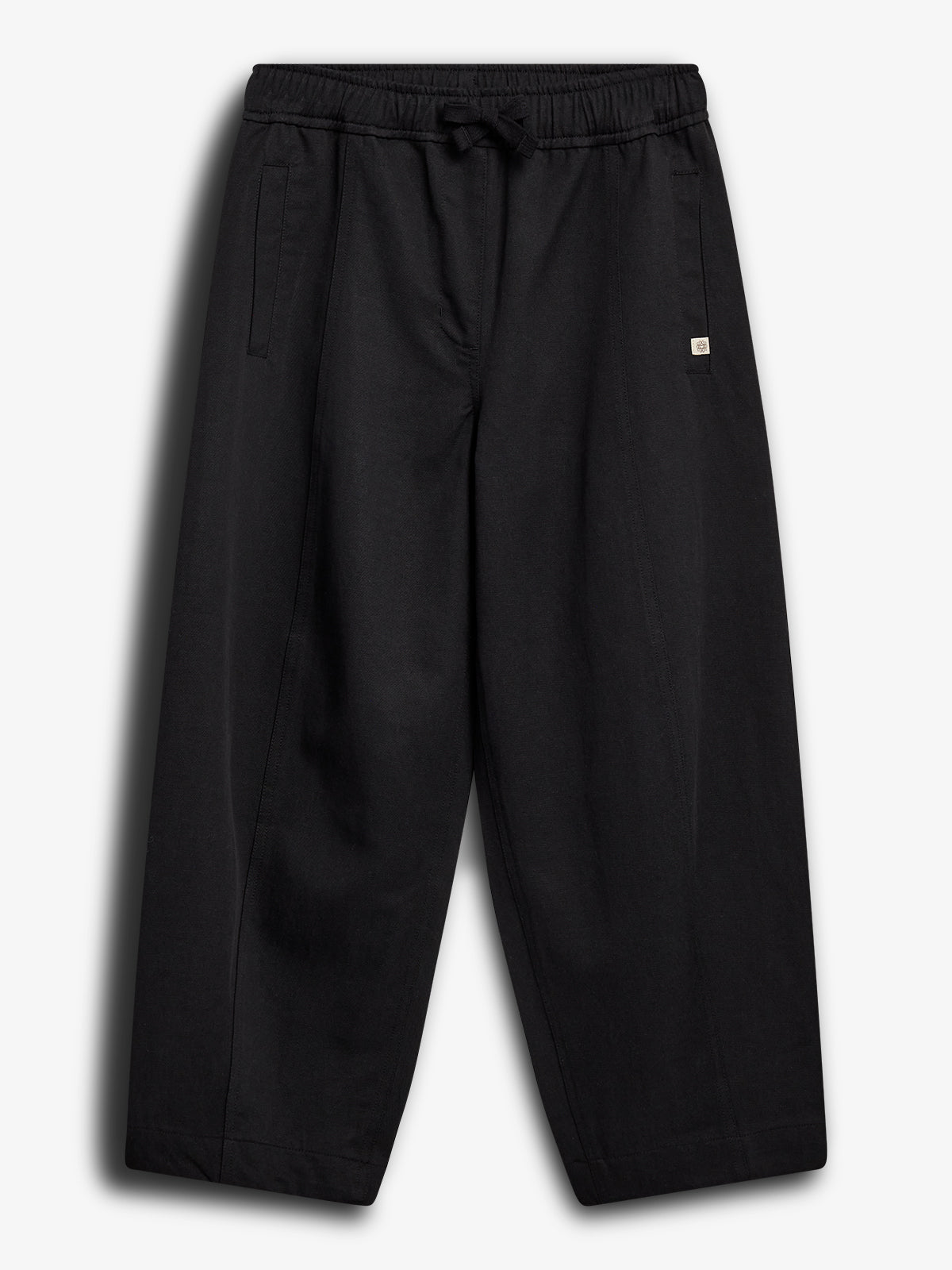Loose black pants hang against a white background. They feature an elastic waistband with a drawstring, side pockets, and a small square logo on the front.