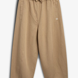 Beige pants with an elastic waistband and drawstring are laid flat. They feature two vertical side pockets and a small patch label. The background is plain white.