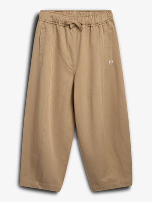 Beige pants with an elastic waistband and drawstring are laid flat. They feature two vertical side pockets and a small patch label. The background is plain white.