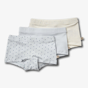 Three pairs of children's underwear lie stacked. The top pair is light blue with small dark dots, beneath are plain light blue and cream pairs. The background is white.