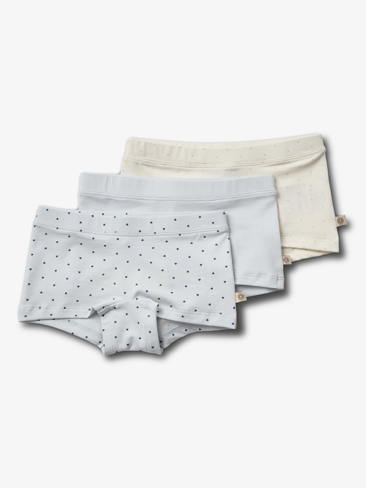 Three pairs of children's underwear lie stacked. The top pair is light blue with small dark dots, beneath are plain light blue and cream pairs. The background is white.