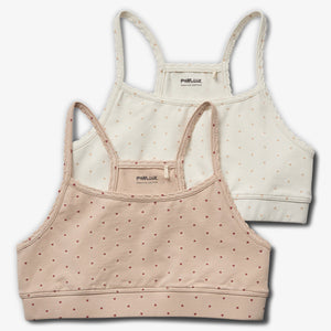 Two polka-dot camisoles with spaghetti straps are layered; one is beige, the other white. Both read "POMP de LUX ORGANIC COTTON" on the interior label. They're on a plain white surface.