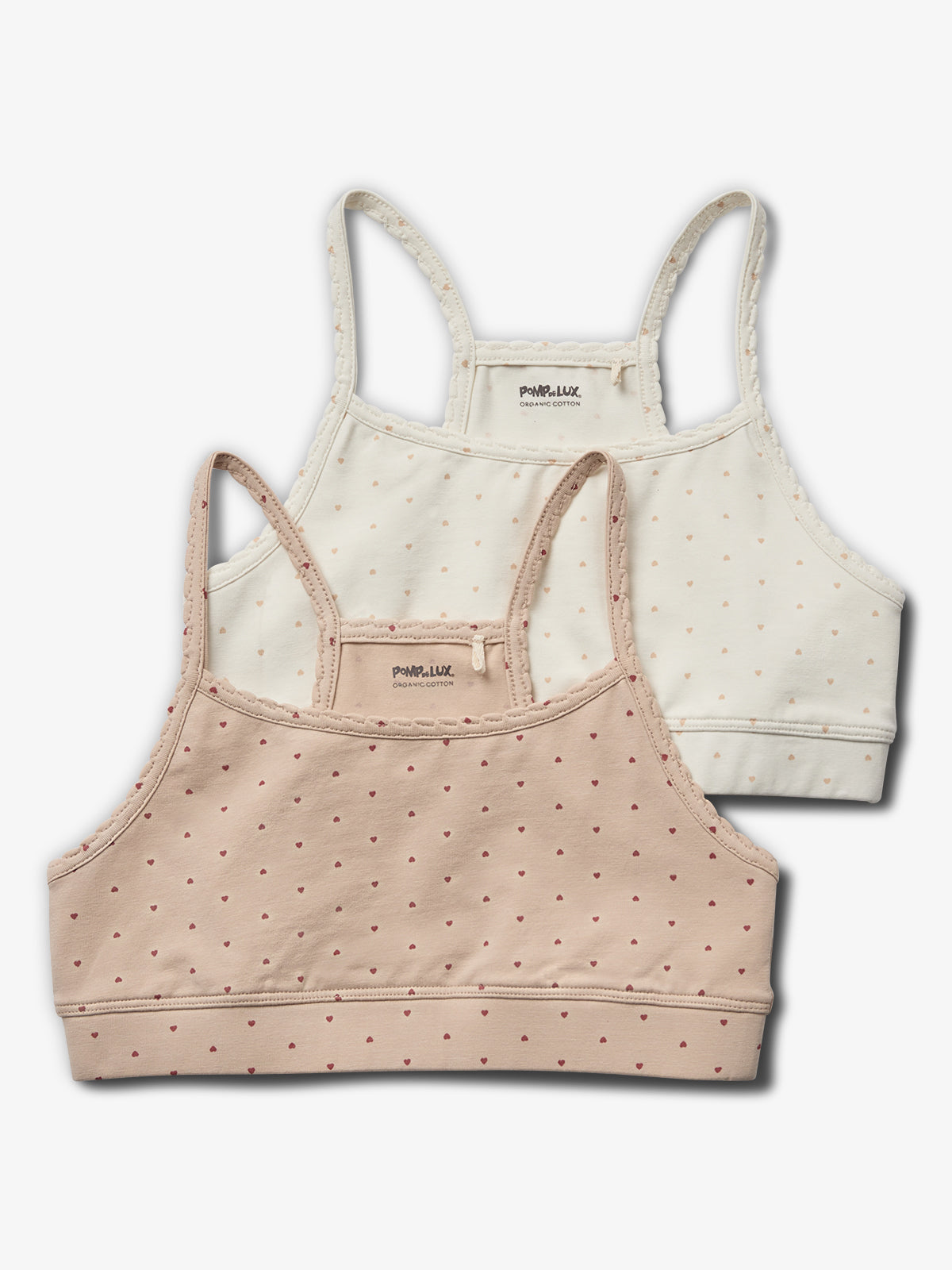 Two polka-dot camisoles with spaghetti straps are layered; one is beige, the other white. Both read "POMP de LUX ORGANIC COTTON" on the interior label. They're on a plain white surface.