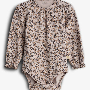 A long-sleeve baby onesie displays a floral pattern in brown and black on a light background. The garment has ruffled cuffs and is labeled “POMPdeLUX ORGANIC COTTON.”