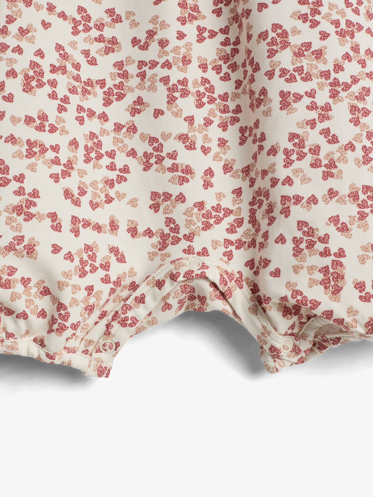 Fabric with a floral pattern features small, scattered red and pink flowers on a light beige background. The hem shows buttons, suggesting it is part of a garment.