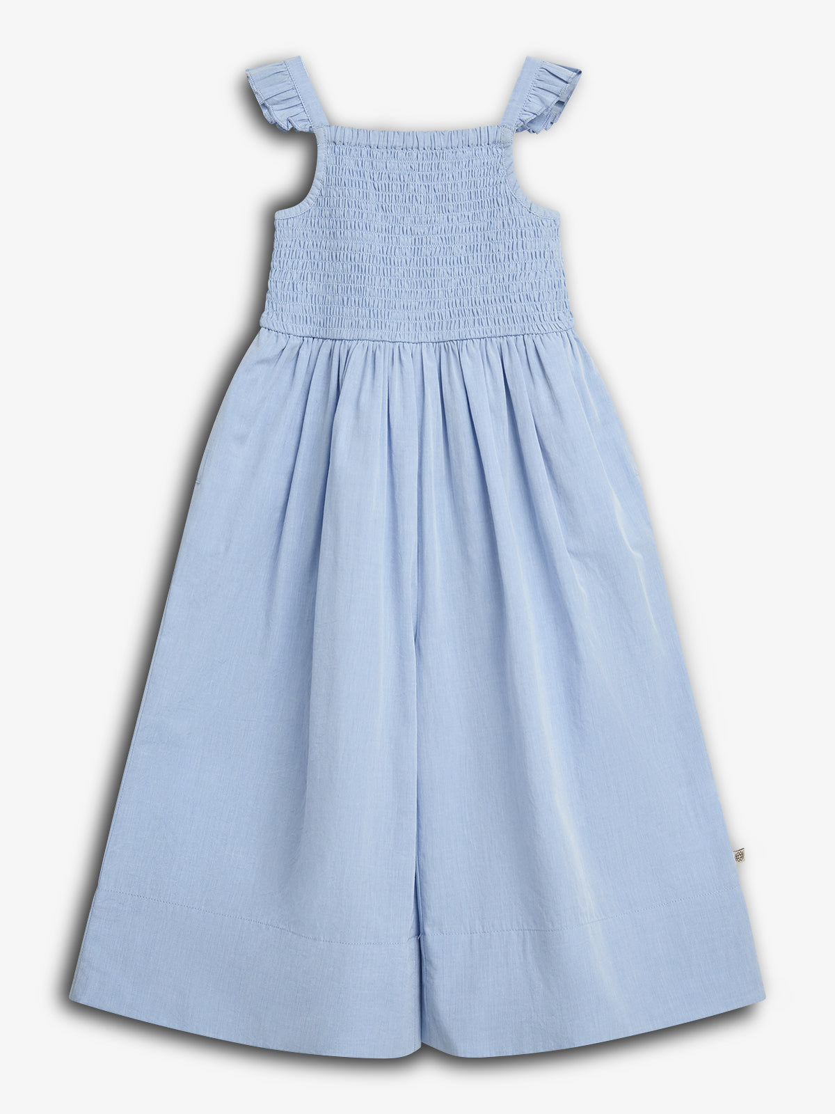 Blue sundress with smocked bodice and ruffled shoulder straps, resting against a plain white background. The dress is sleeveless and features wide, flowing pants for a relaxed fit.