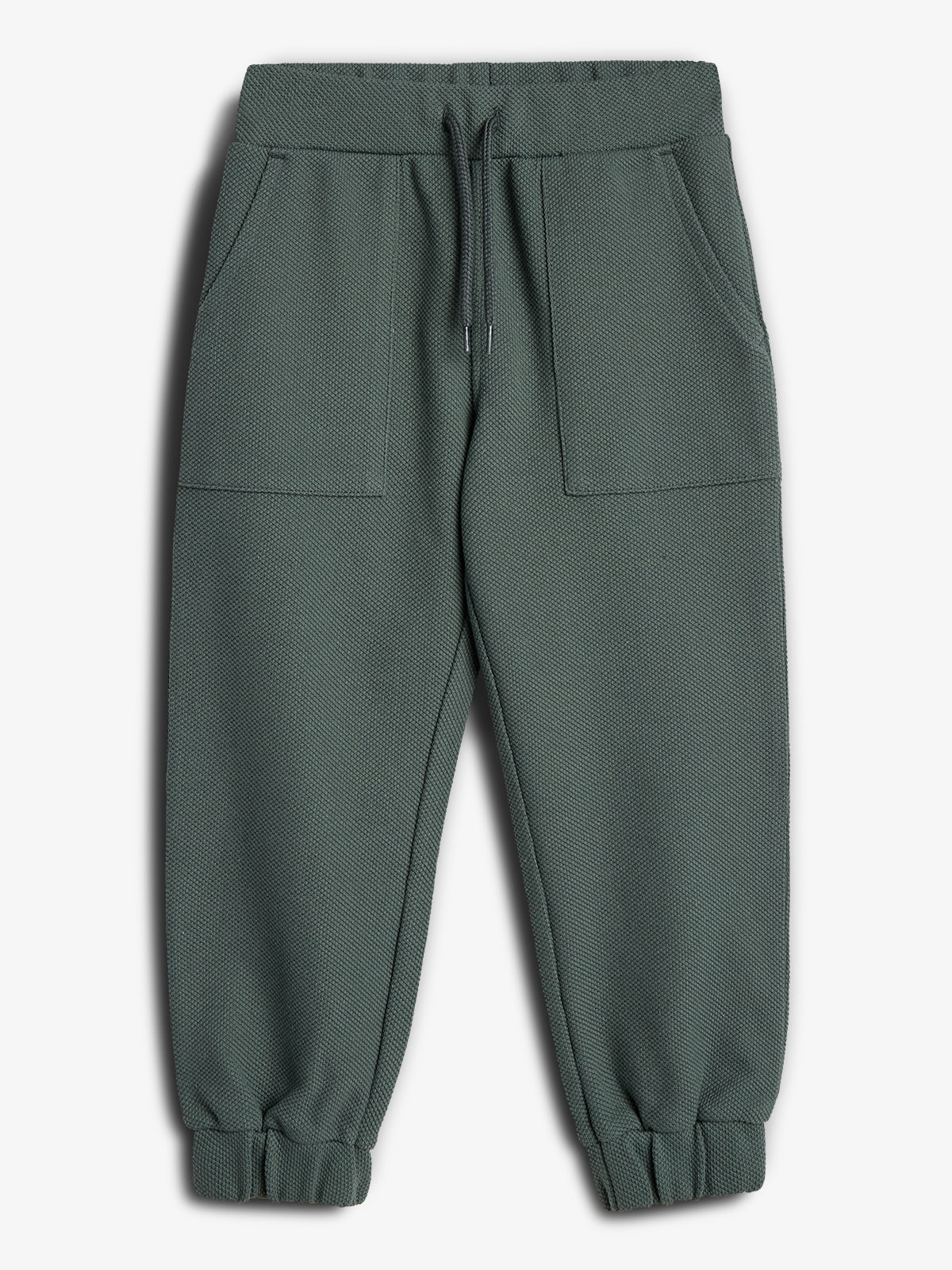 Green sweatpants with a textured fabric and an elastic waistband feature drawstrings for adjustment. They have two large front pockets and elastic cuffs, set against a plain white background.