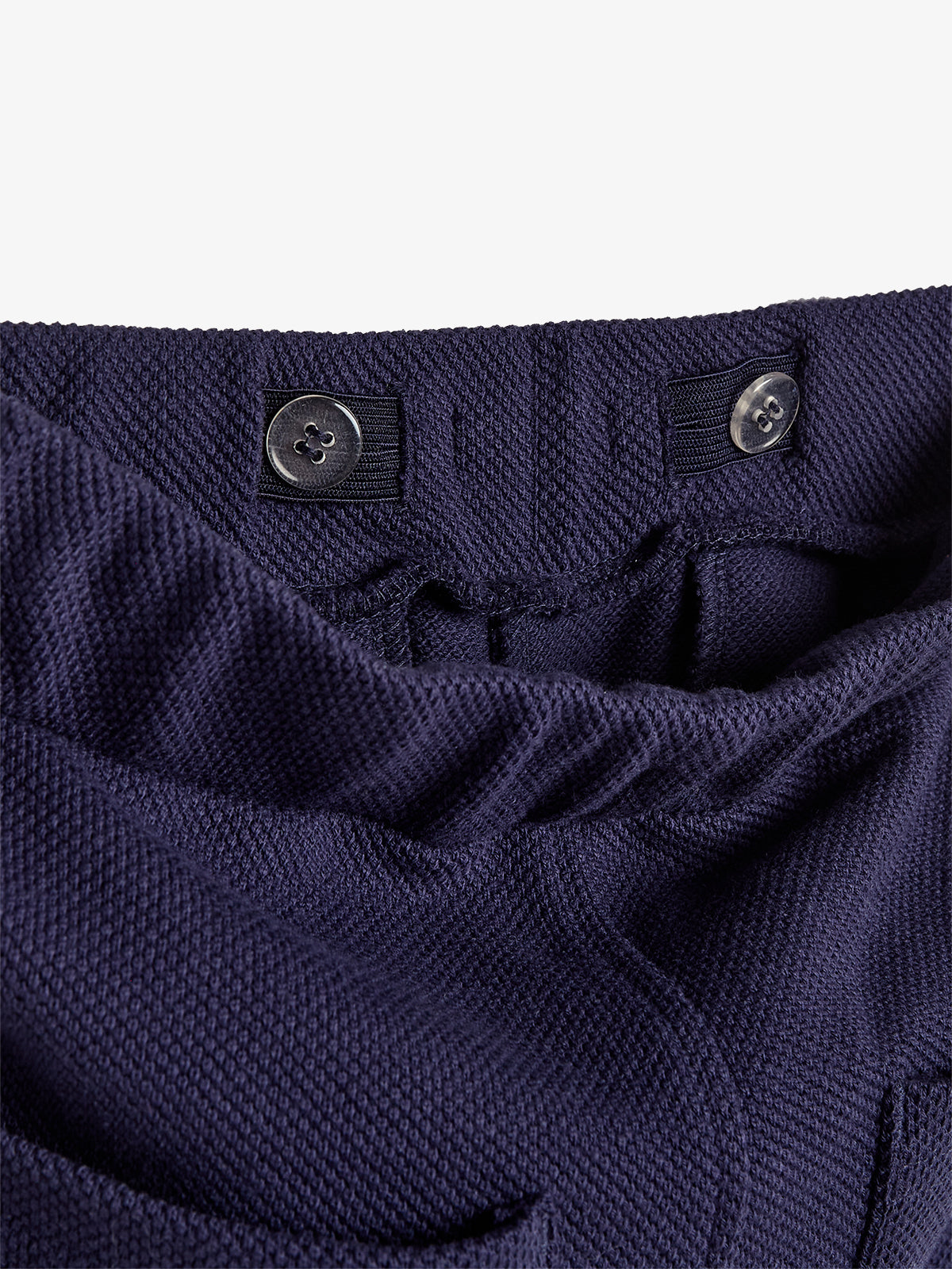 Blue fabric with textured weave forms a waistband, featuring two black buttons on elastic bands. The fabric is gathered, indicating adjustable functionality. The close-up shows detail without other surroundings.