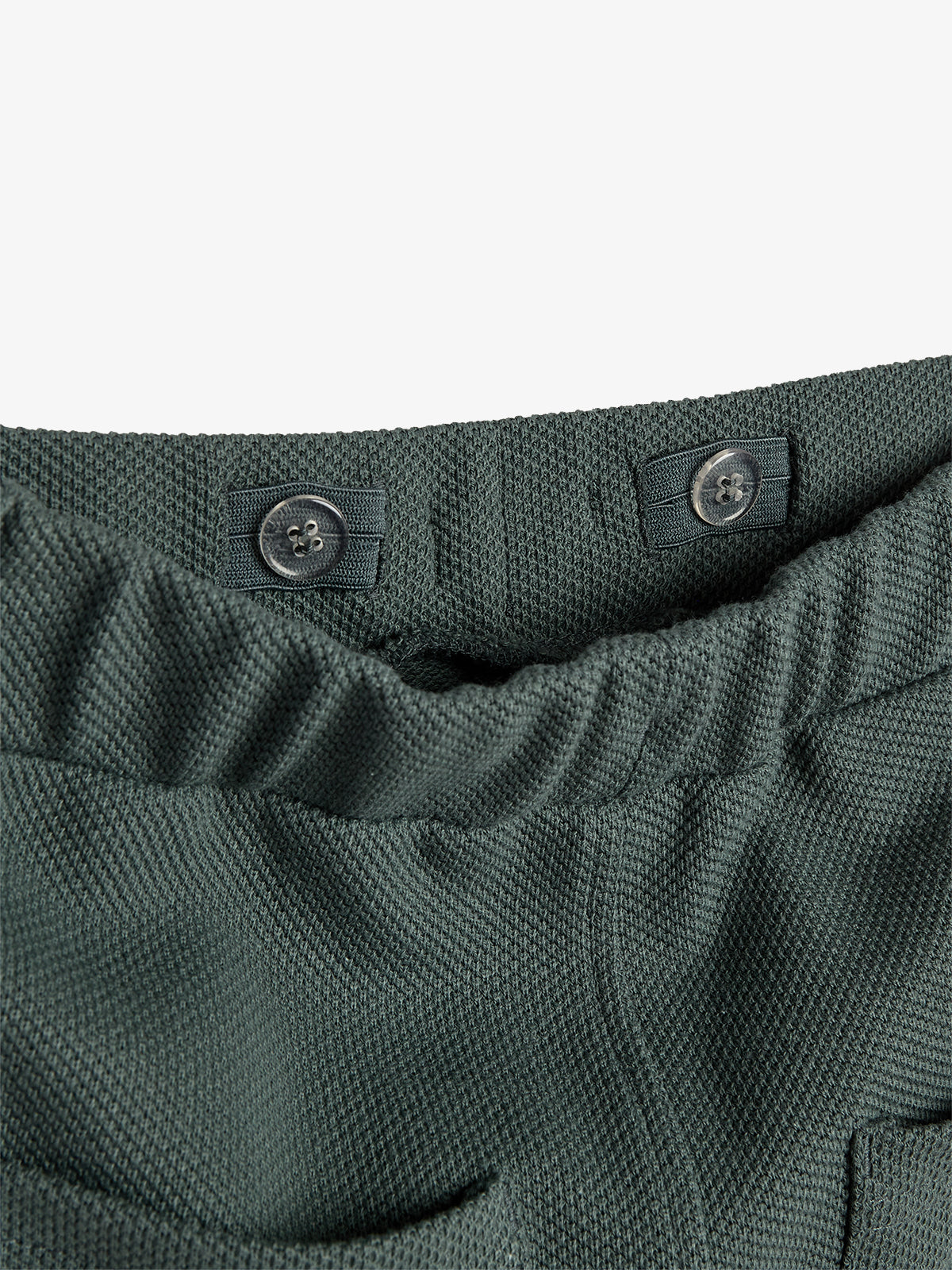 A dark green elastic waistband features two black buttons and textured fabric, shown in close-up against a plain white background.
