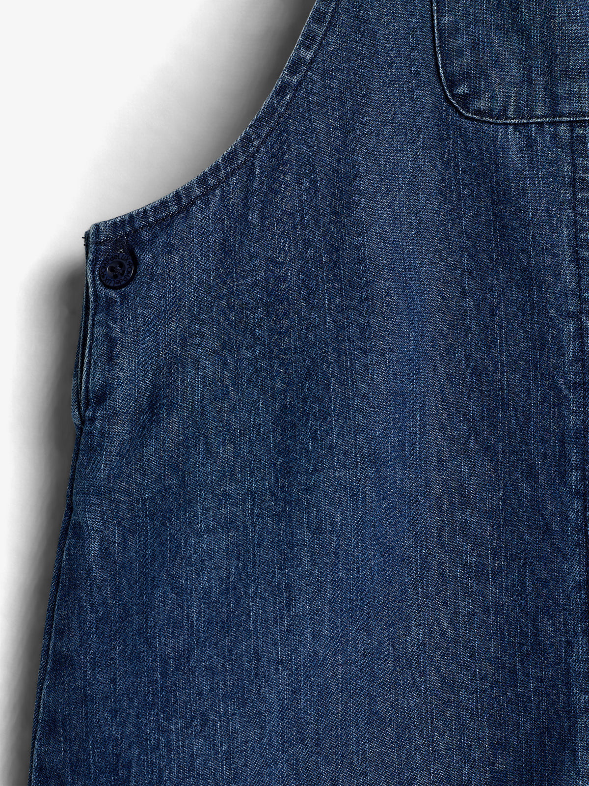 Denim fabric with a visible button and stitching detail, shown closely against a neutral background, highlighting the texture and weave of the material.