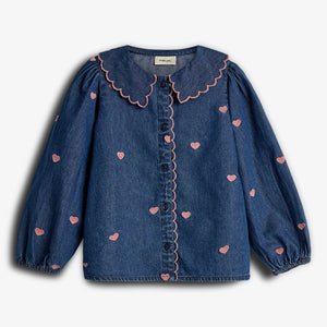 A blue denim blouse features pink heart patterns and a scalloped collar. It has long sleeves with elastic cuffs and a button-down front. The style appears playful and romantic.
