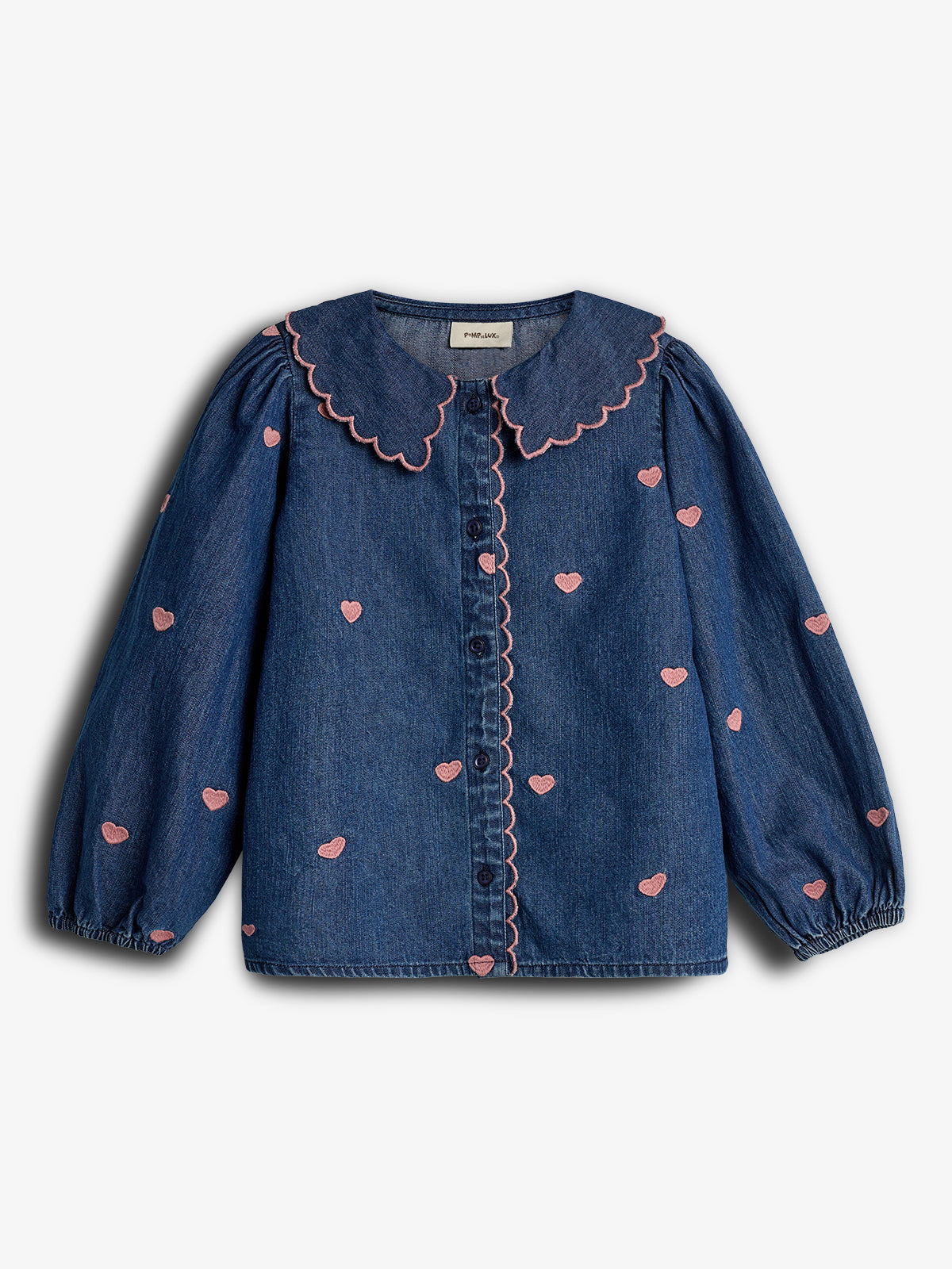 A blue denim blouse features pink heart patterns and a scalloped collar. It has long sleeves with elastic cuffs and a button-down front. The style appears playful and romantic.