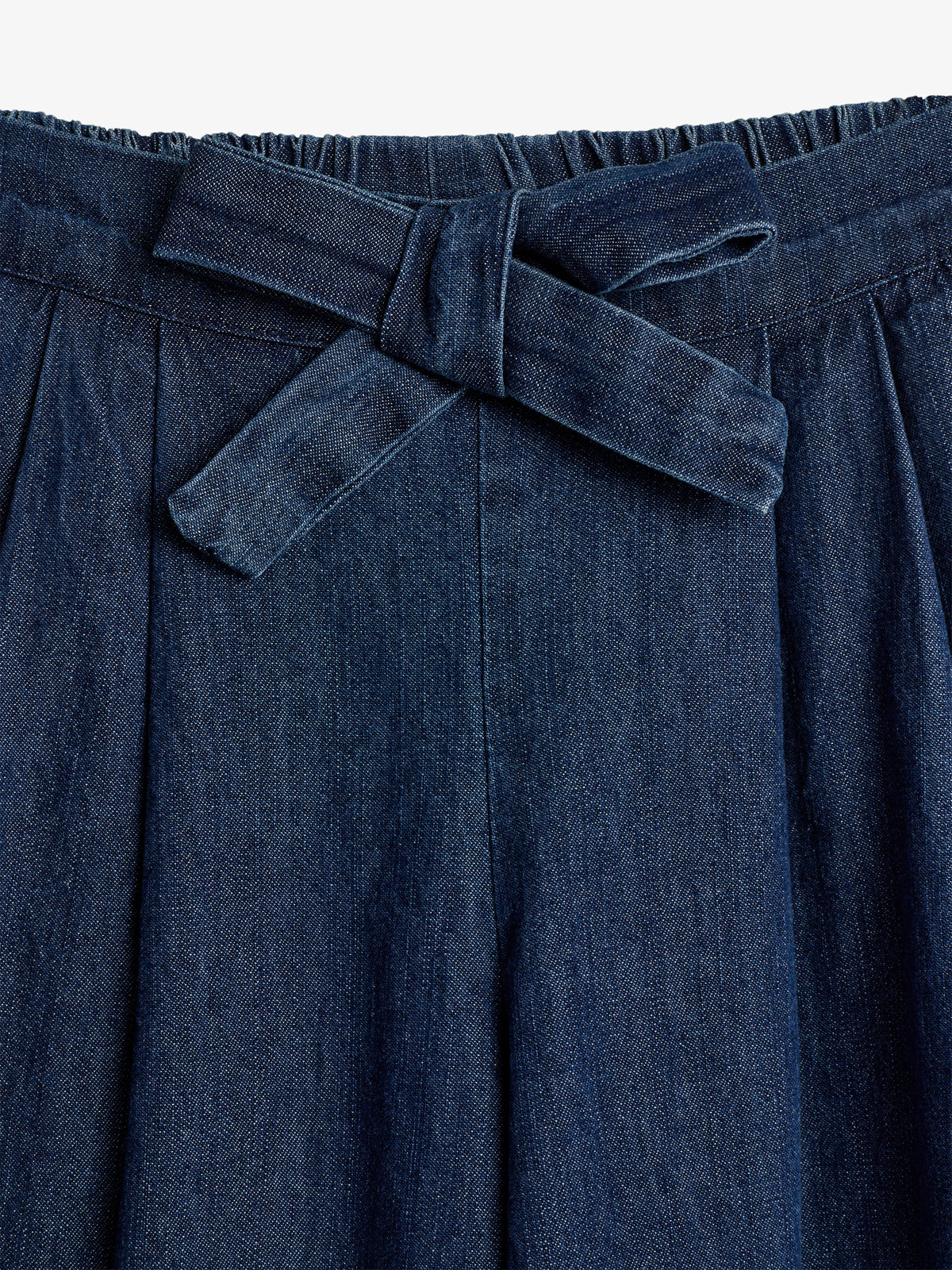 Dark denim fabric forms pleated pants with a visible waistband, featuring a tied belt. The texture and deep blue color are prominent, suggesting casual or semi-formal wear.