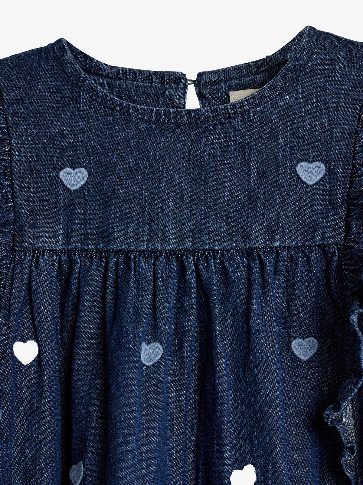 Denim dress featuring embroidered heart patterns, gathered at the waist, with a back button closure. The background is plain white, highlighting the dress's design details.