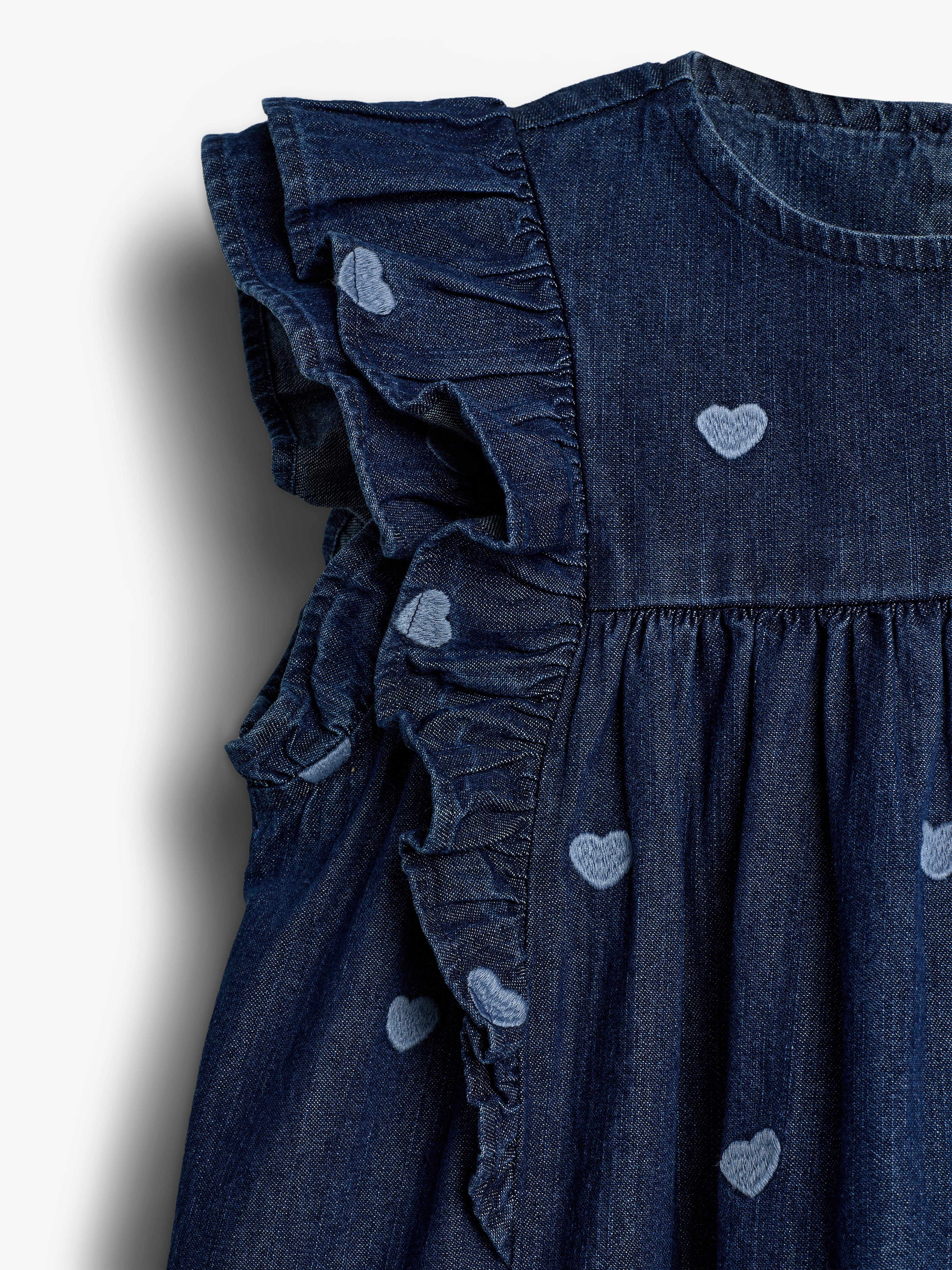 Denim dress with ruffled sleeves, adorned with embroidered light blue hearts. The fabric has a gathered design below the round neckline, creating a textured, elegant appearance.