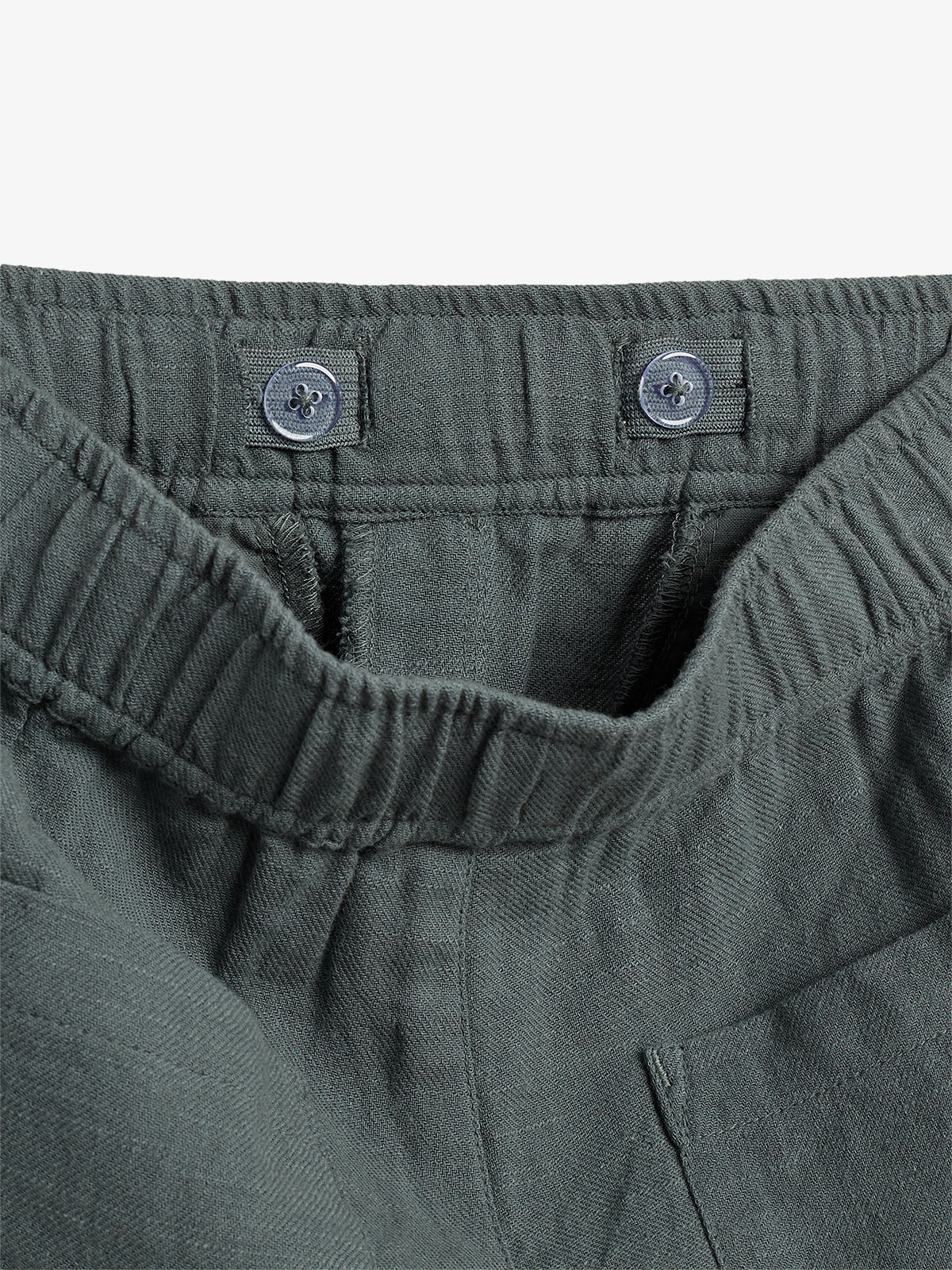 Green elastic waistband with two buttons visible; fabric appears gathered, set against a plain background.