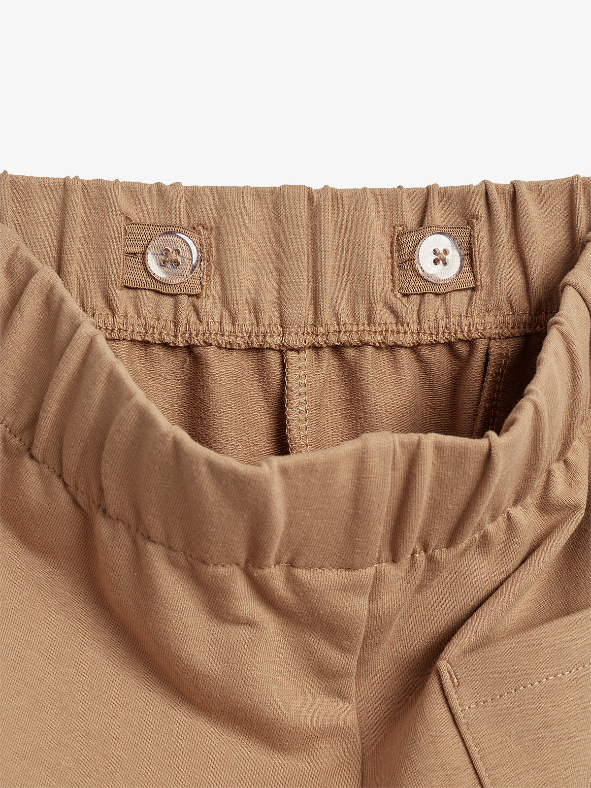 Brown elastic waistband with adjustable buttons on fabric tabs, part of a garment. The material appears smooth, and the stitching is visible, creating a textured appearance.
